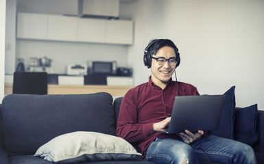 Young man working on laptop in home wearing headphones